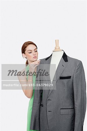Junge weibliche Modedesignerin betrachten Blazer auf Schneider ist gegenüber dem grauen Hintergrund Attrappe