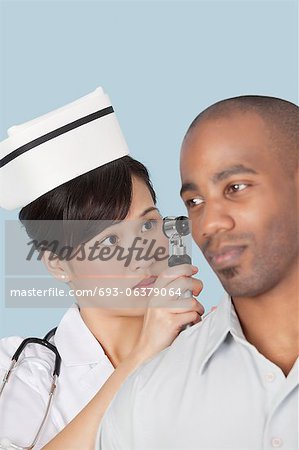 Infirmière examinant l'oreille du patient masculin sur fond bleu clair