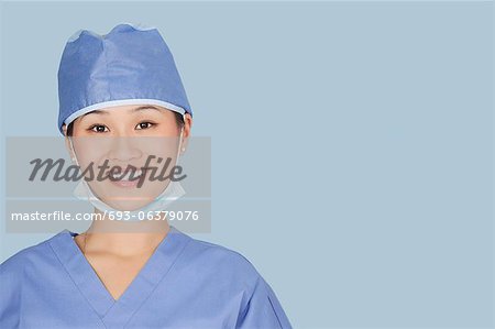 Close-up portrait of female surgeon smiling over light blue background