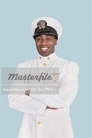 Portrait d'un jeune officier de marine américaine heureux debout avec les bras croisés sur fond bleu clair