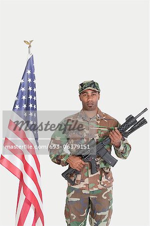 Portrait of soldier with M4 assault rifle standing by American flag, Studio Shot on gray background