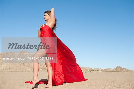 Toute la longueur d'une jeune femme enveloppée dans un tissu rouge sur le paysage aride