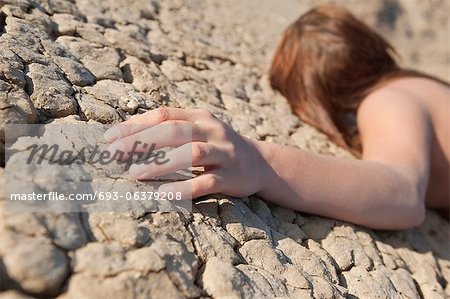Woman lying on cracked land with focus on hand