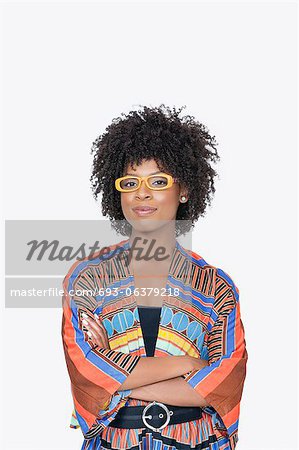 Portrait de jeune femme en tenue imprimé africain, debout les mains jointes sur fond gris