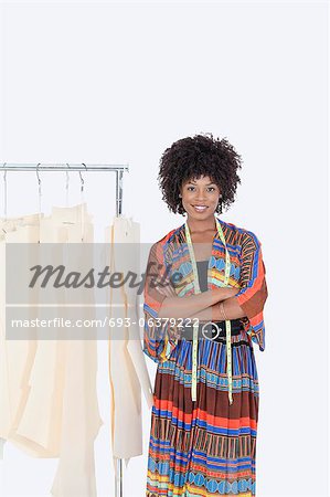 Portrait of an African American female designer with sewing patterns on clothes rack over gray background