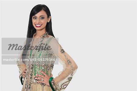 Porträt einer indischen Frau im eleganten Designer tragen stehend mit den Händen an den Hüften über grauen Hintergrund