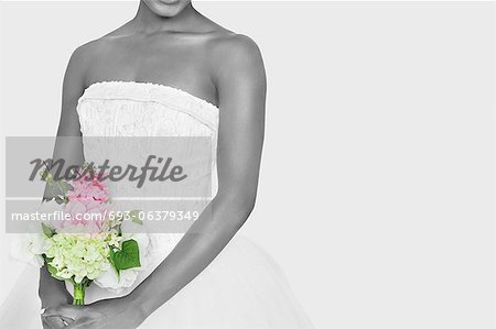 Midsection of bride holding bouquet over gray background