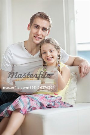 Portrait du père et fille, regarder la télévision avec un bol plein de roue forme snack pellets