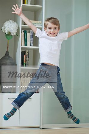 Portrait d'un garçon en employés occasionnels sautant dans les airs à la maison