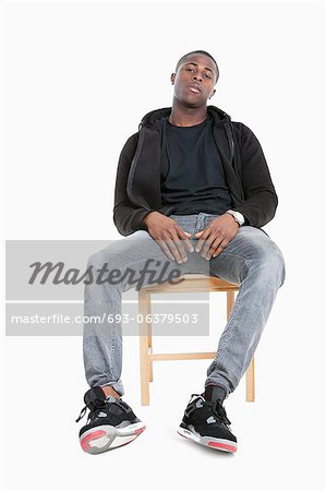 Portrait of a trendy African American man sitting on chair over gray background
