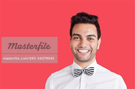 Portrait of a happy mid adult man wearing bow-tie over red background