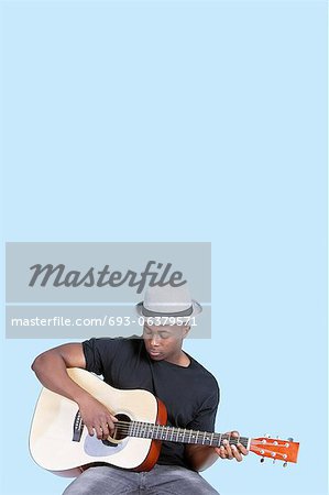 Young African American man playing guitar over light blue background