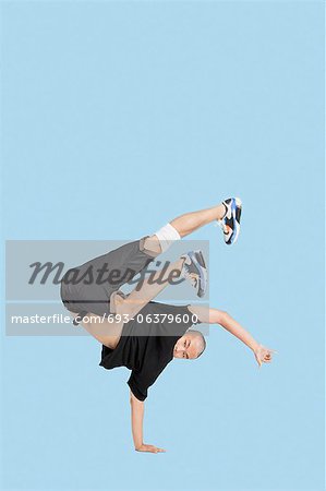 Male break dancer performing handstand over blue background