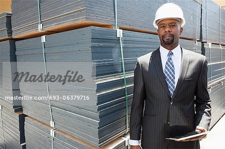 Portrait of African American male contractor holding tablet PC by stacked wooden planks