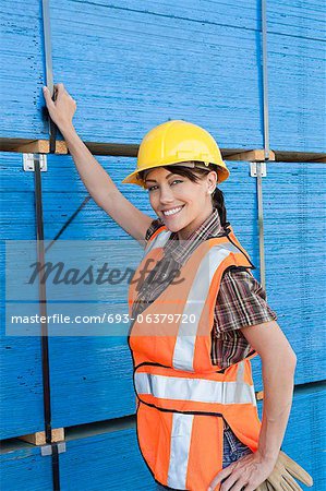 Portrait of female industrial worker standing by stacked wooden planks