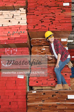 Asian female industrial worker standing on stacked wooden planks holding tablet PC