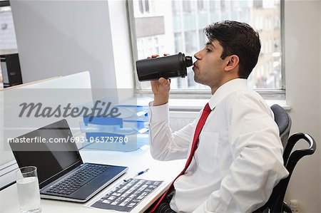 Side view of an Indian businessman drinking water at office desk