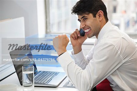 Heureux homme d'affaires à l'aide de téléphone portable au PC de bureau