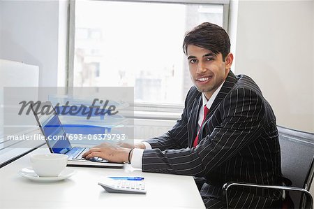 Portrait of an Indian businessman writing on paper at desk in office