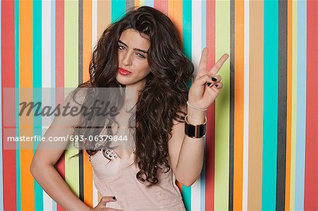 Portrait of a woman gesturing victory sign against colorful striped background