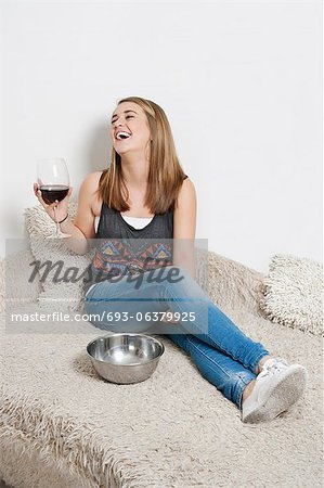 Happy young woman with wine glass sitting on sofa