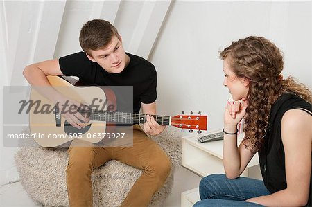 Young man strumming guitar besides female friend