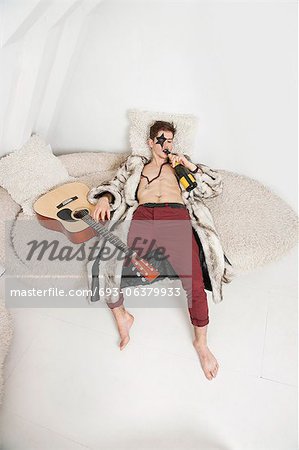 Jeune homme avec guitare boire en position couchée sur le canapé