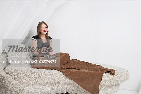 Jeune femme au lit maintenant la télécommande souriante Jeune femme au lit maintenant la télécommande souriante
