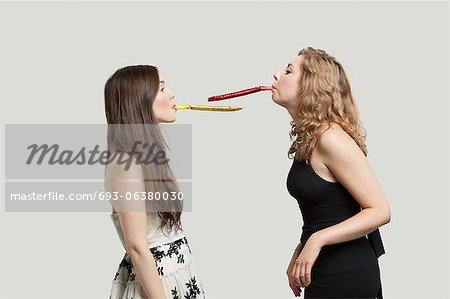 Two young women blowing party puffers while looking at each other against gray background