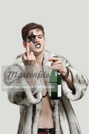 Portrait de jeune homme avec un geste grossier tout en tenant la bouteille de bière sur fond gris