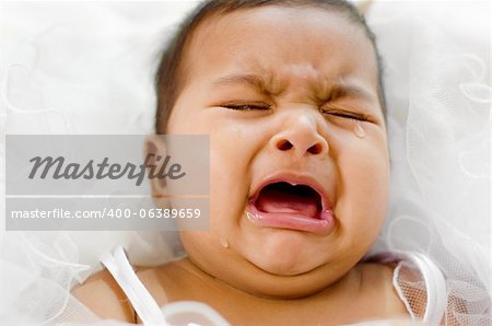 Crying Indian baby girl lying on bed