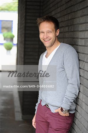 Smiling man leaning against brick wall