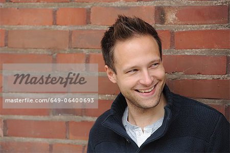 Homme souriant, appuyé contre le mur de briques