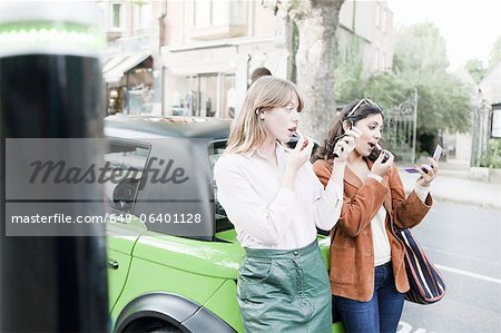 Women applying lipstick on city street