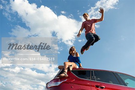 Jeune homme sautant de toit de voiture, fille assise sur le toit