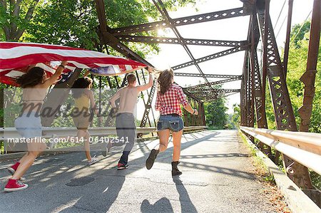 Group of friends running on bridge holding american flag