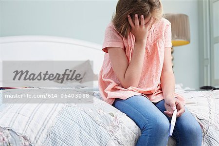 Jeune fille assise sur le lit avec le test de grossesse
