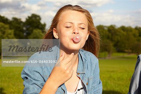 Teenage girl in park, blowing bubble gum