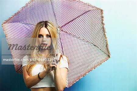 Porträt einer jungen Frau mit Sonnenschirm vor blauem Hintergrund