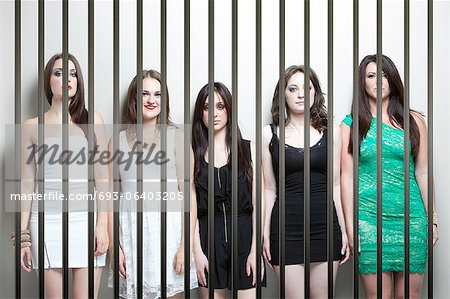 Portrait of five young women standing side by side behinds prison bars