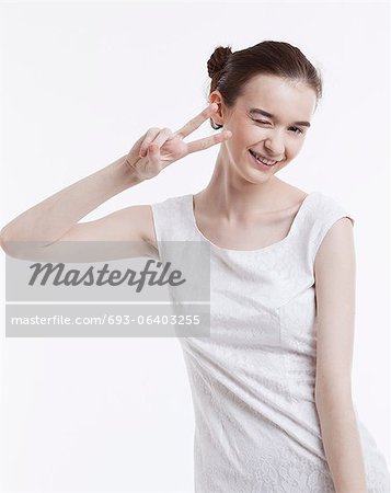 Portrait of young woman in dress gesturing peace sign over white background