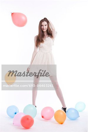 Beautiful young woman in dress with balloons on floor against white background