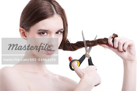 Portrait of beautiful young woman with scissors cutting her hair over white background