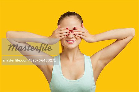 Beautiful young woman covering eyes over yellow background