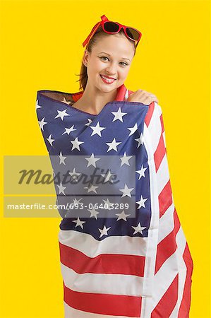 Porträt der jungen Frau glücklich umwickelt amerikanische Flagge auf gelbem Grund