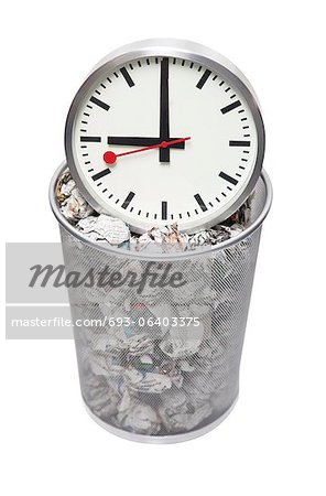 Clock in wastebasket full of crumpled paper over white background