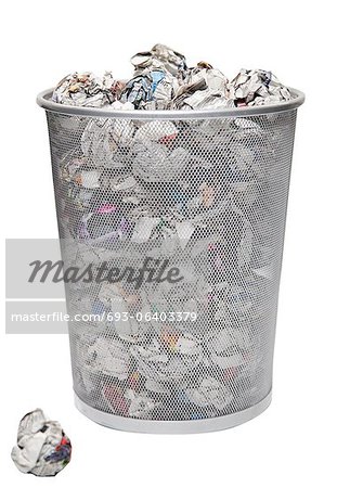 Wastepaper basket with papers lying over white background
