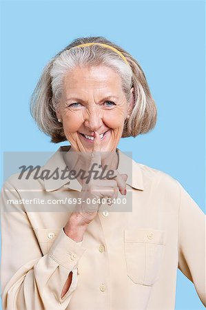 Portrait d'une femme senior souriante en employés occasionnels avec le doigt sur les lèvres sur fond bleu