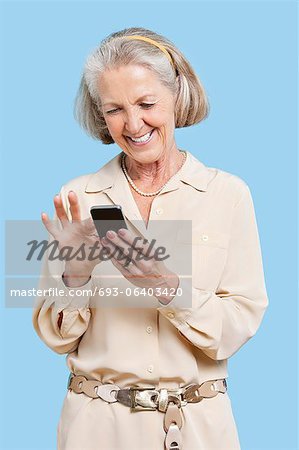 Smiling senior woman reading text message on cell phone against blue background