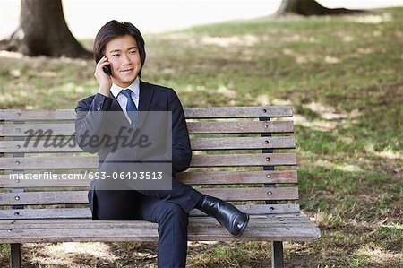 Young businessman using cell phone while sitting on bench at park